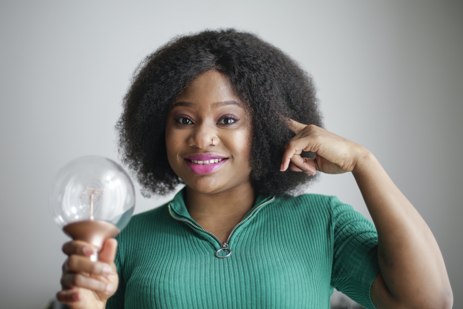Positive young African American lady holding light bulb in hand on gray background